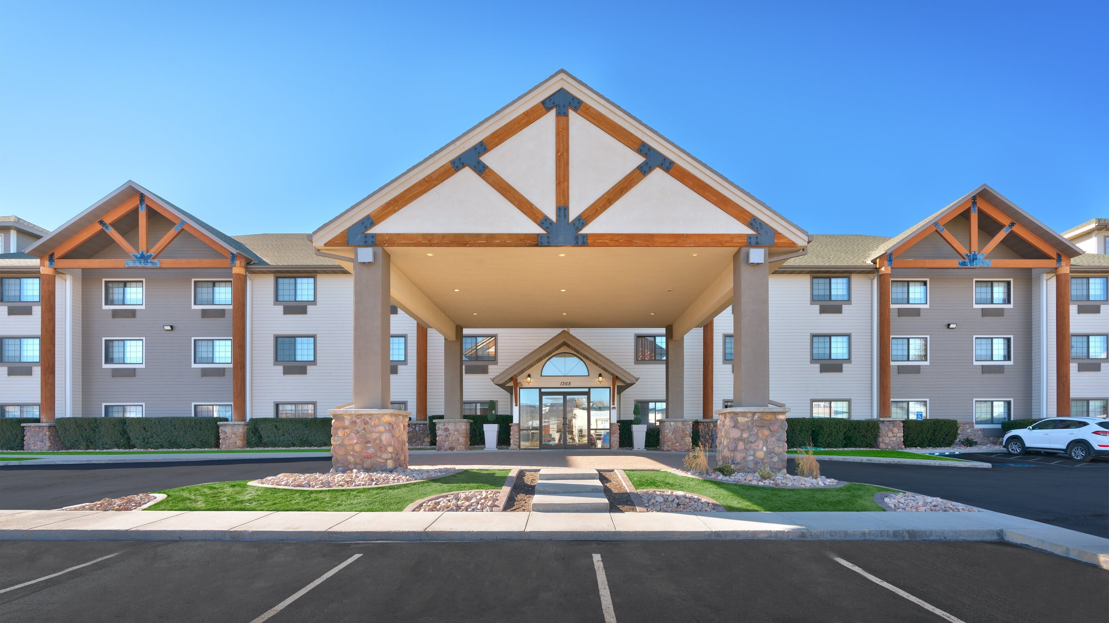 A multi-story hotel with a central entrance, outdoor parking, and a landscaped area with stone pillars.