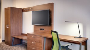 Um espaço de escritório moderno com uma mesa de madeira, uma cadeira, uma TV fixada na parede e um abajur.