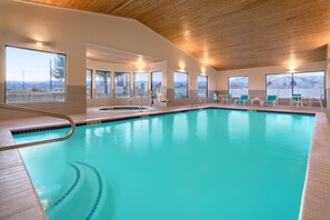 A large indoor swimming pool with clear blue water, surrounded by lounge chairs and a view of a mountainous landscape through large windows. - Holiday Inn Express Heber City by IHG (Heber City)