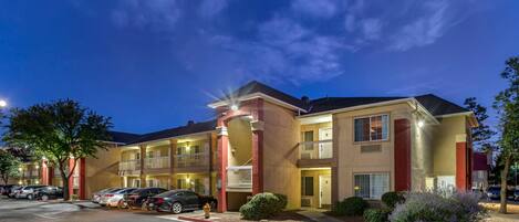 A multi-story hotel with a parking lot, outdoor lighting, and a clear sky.