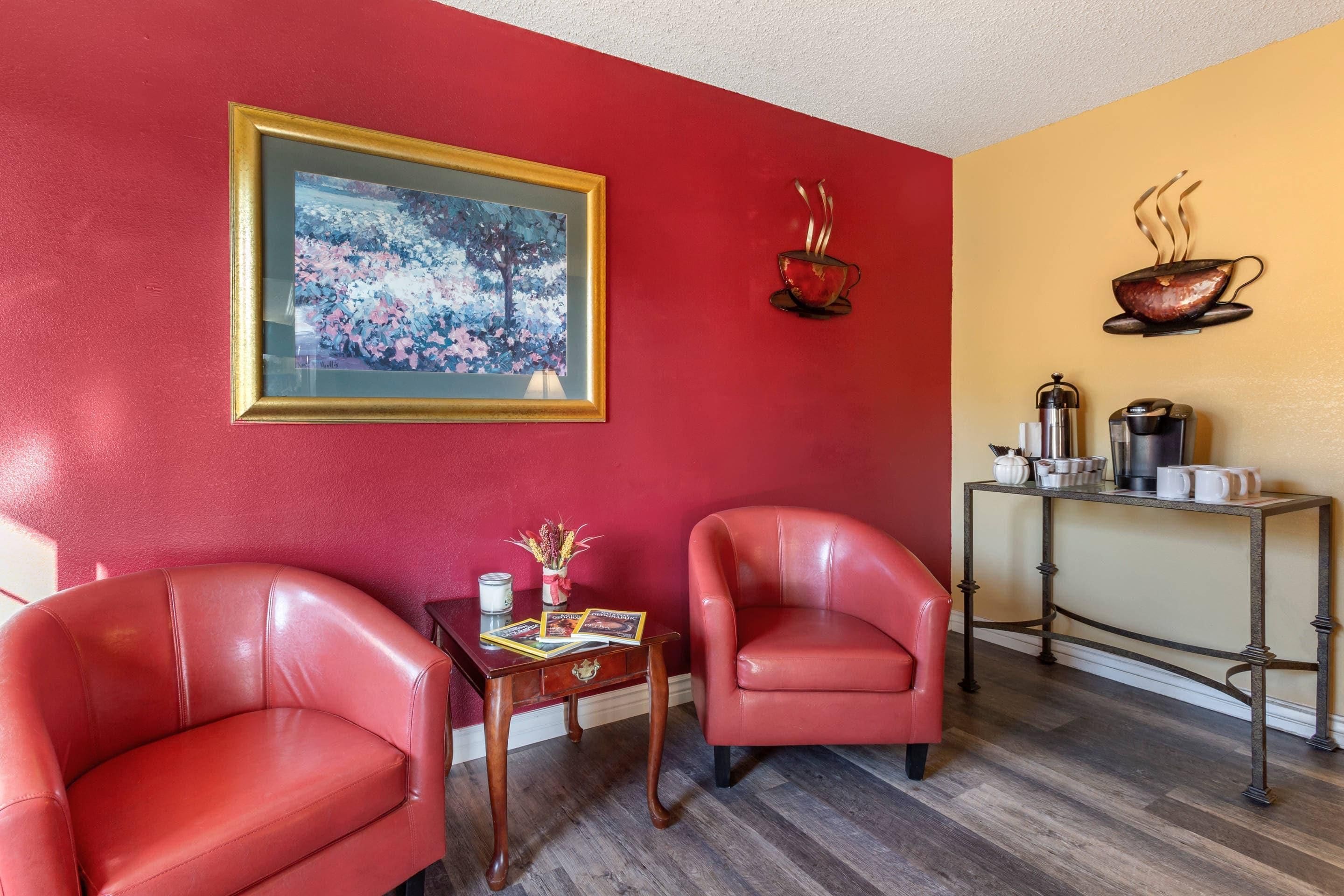 A room with two leather chairs, a table with a vase and candles, a framed painting, and a coffee station.
