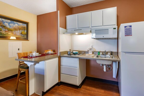 A compact kitchen with white cabinets, a microwave, a sink, and a refrigerator. - Suburban Studios Albuquerque Uptown (Albuquerque)