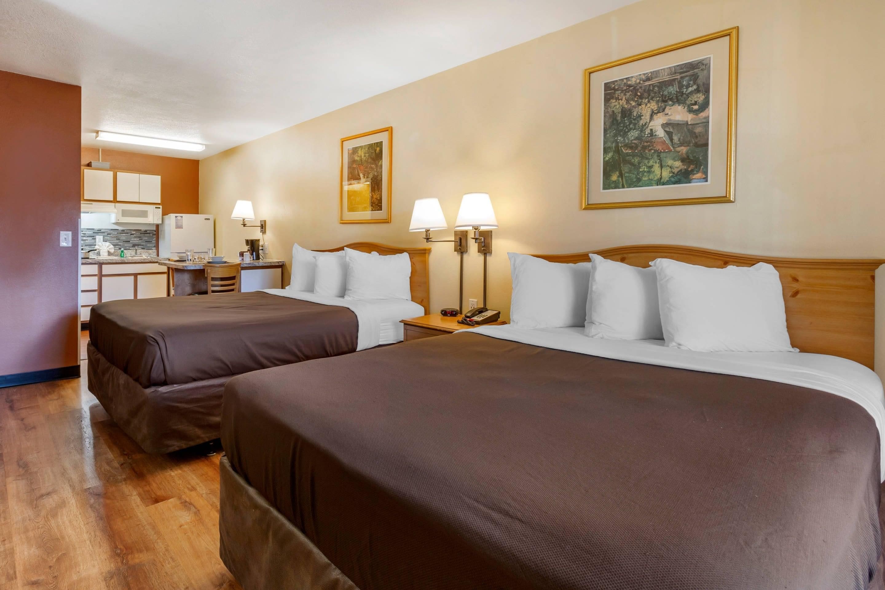 A hotel room with two beds, a kitchenette, and artwork on the walls.