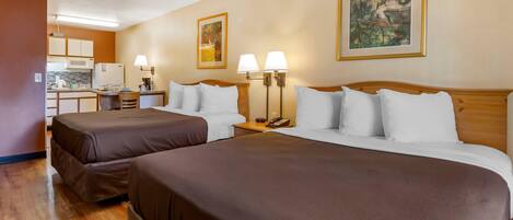 A hotel room with two beds, a kitchenette, and artwork on the walls.