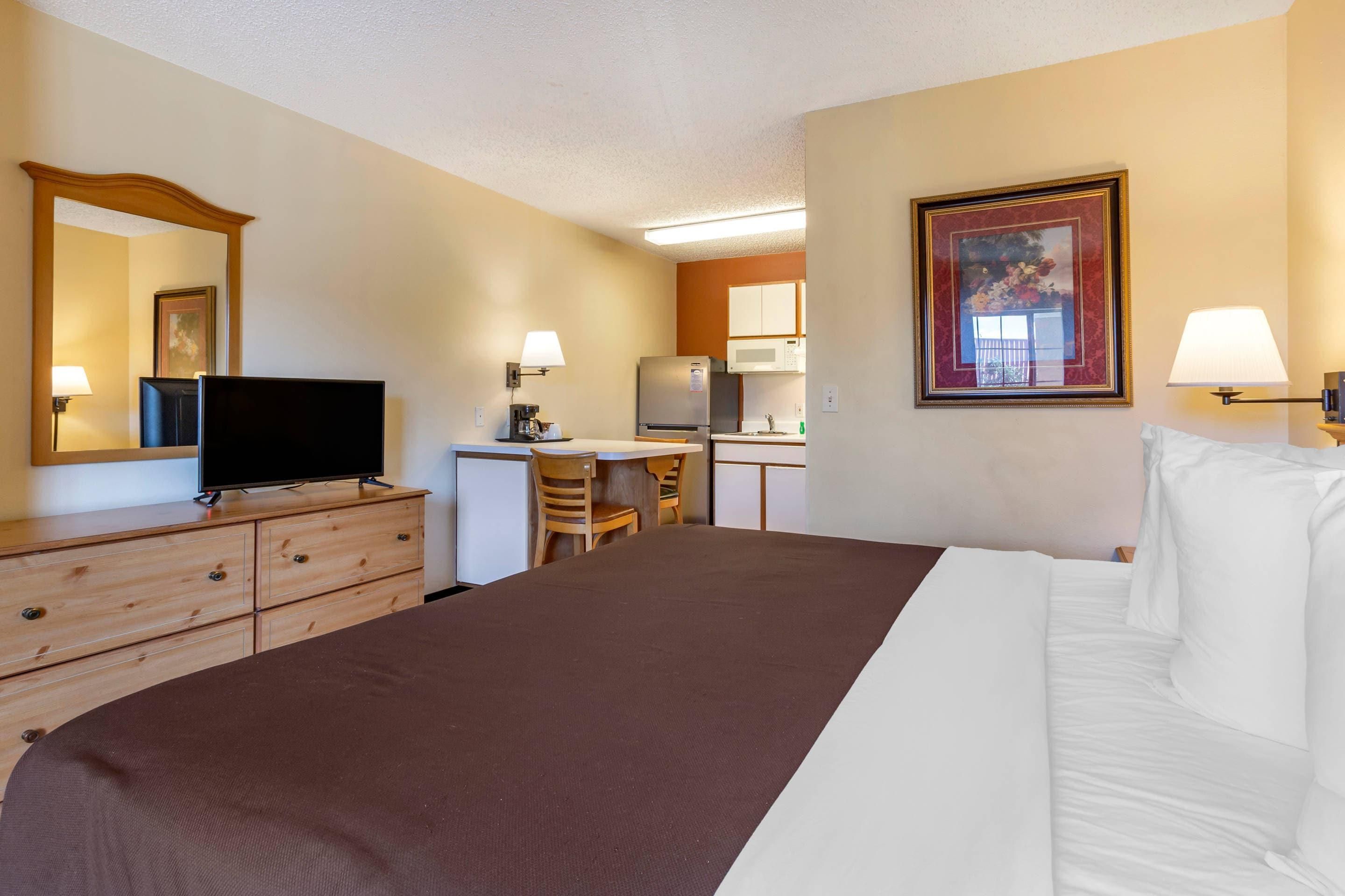 A hotel room with a bed, a desk, a television, a dresser, and a painting on the wall.