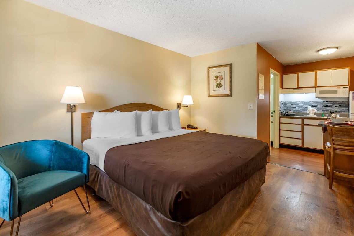 A hotel room with a large bed, a desk, a chair, and a kitchenette.