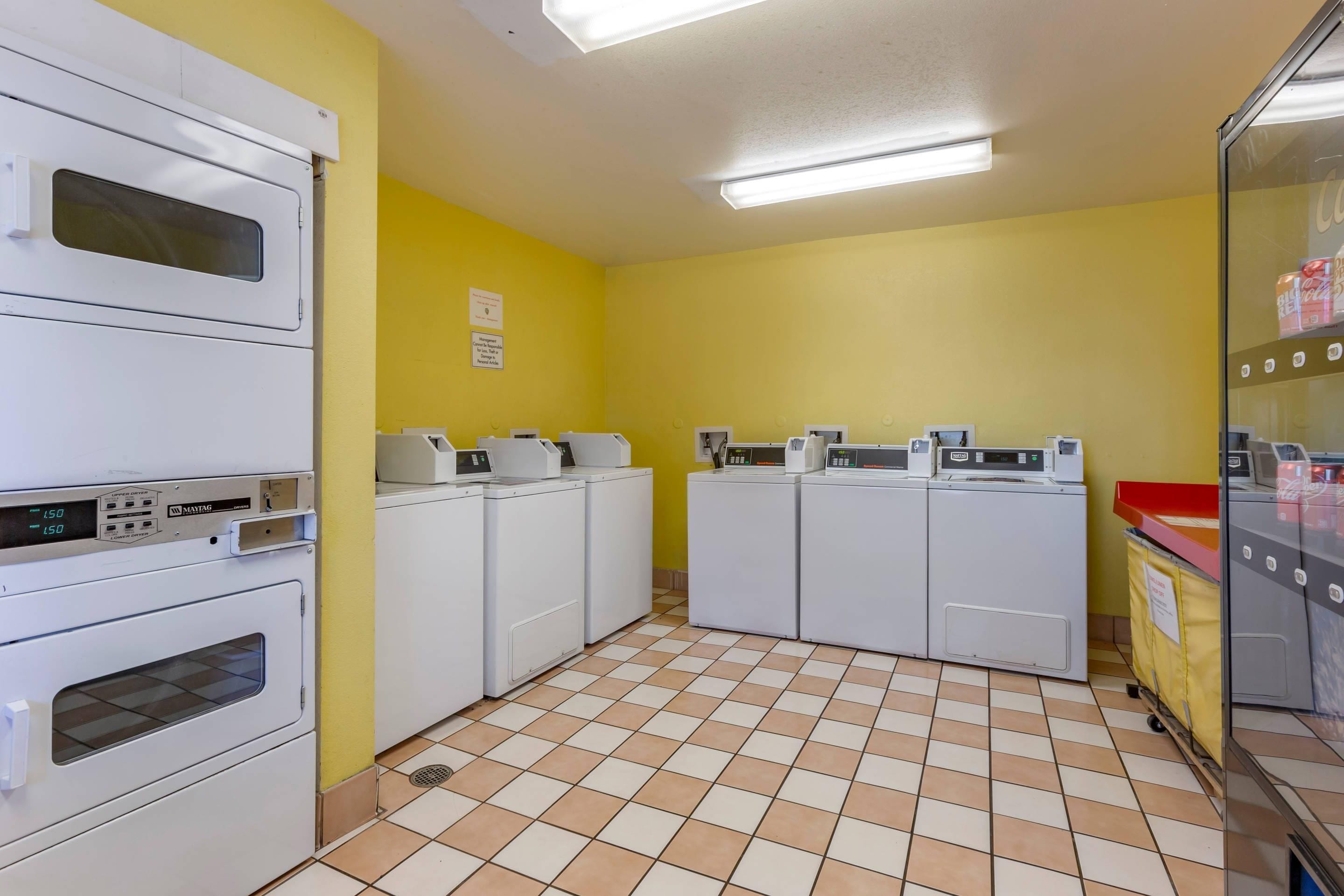 A laundry facility with stacked dryers, washing machines, and a yellow wall.