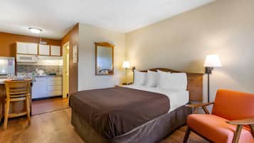 A hotel room with a bed, a chair, a desk, a microwave, and a kitchen area.
