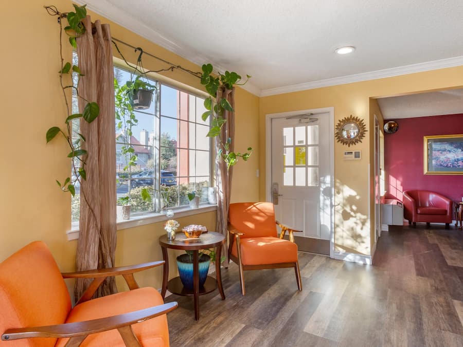 A room with a wooden floor, a red chair, a table with a vase, and a window with curtains.