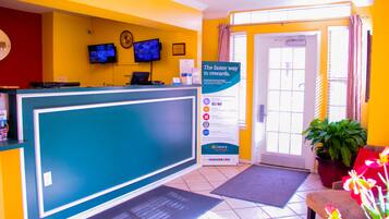 A reception area with a blue reception desk, a television mounted on the wall, a signboard, and a potted plant.