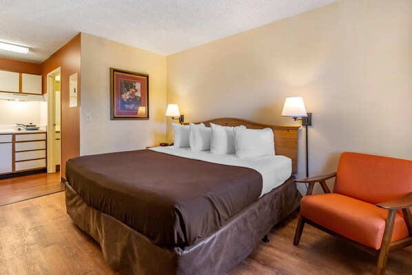 A hotel room with a bed, a chair, a nightstand, a lamp, and a painting on the wall.