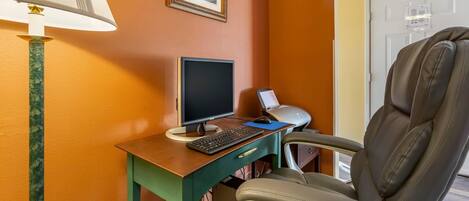 Una habitación con escritorio, computadora, silla, lámpara y un cuadro en la pared.