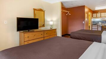 A hotel room with two beds, a TV on a wooden dresser, a mirror, and a kitchenette.