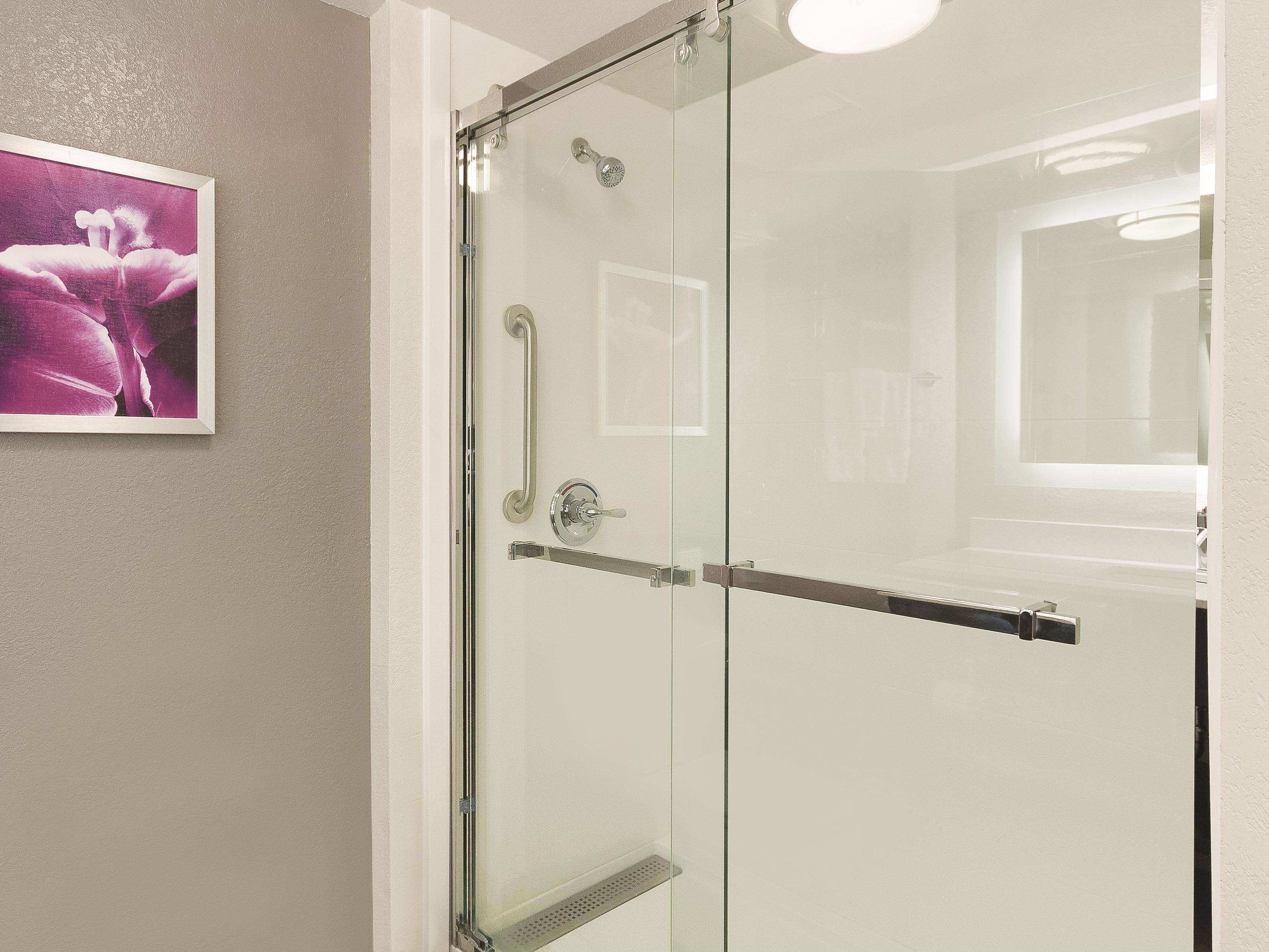 A glass-enclosed shower with a handrail, a door with a handle, and a small shelf.