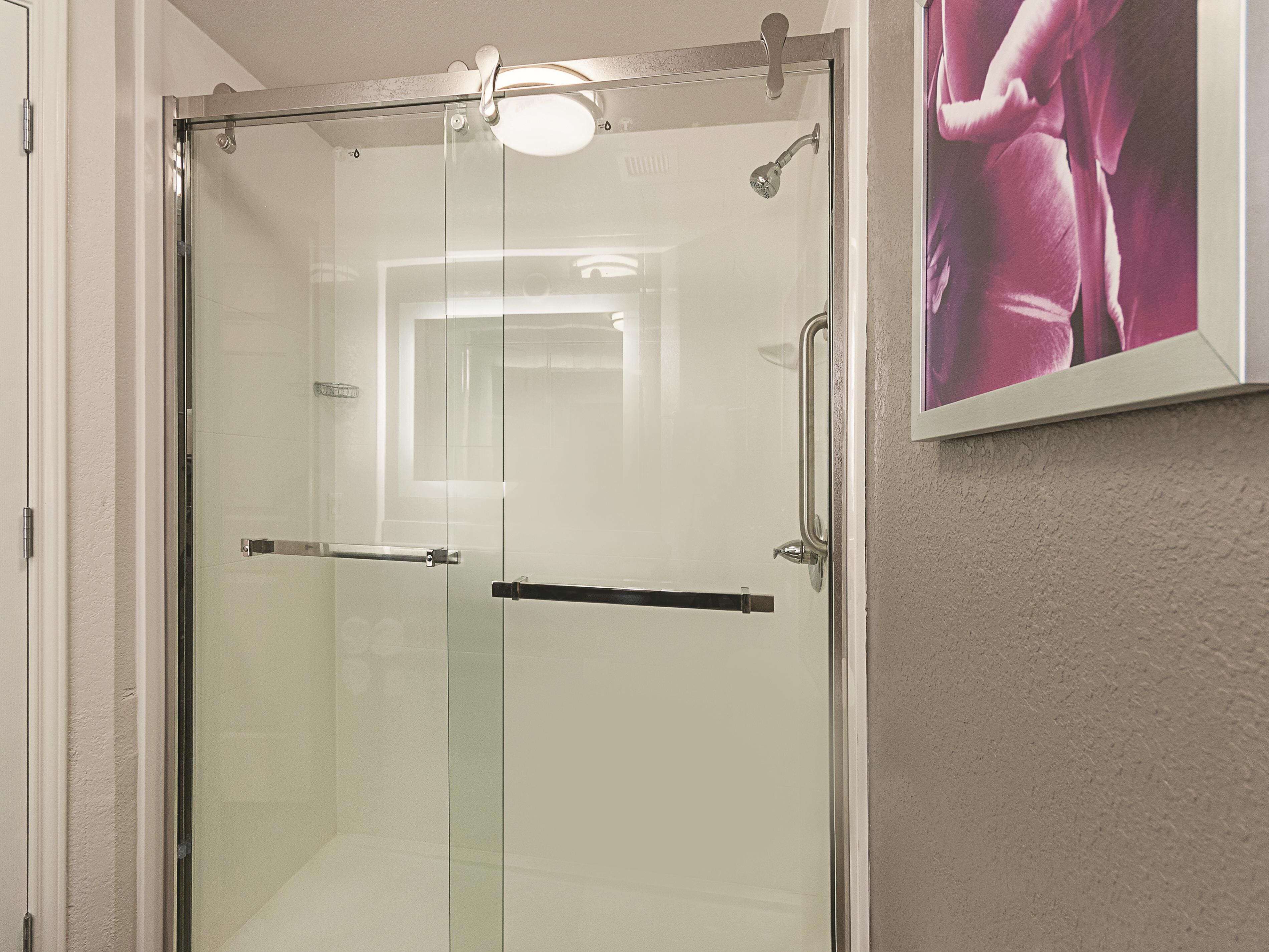 A glass-enclosed shower stall with a handheld showerhead and a handheld shower attachment.