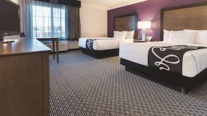 Habitación de hotel con dos camas, un escritorio y una ventana con cortinas.