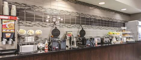 A modern kitchen with a waffle maker, coffee machine, and various food items on the counter.