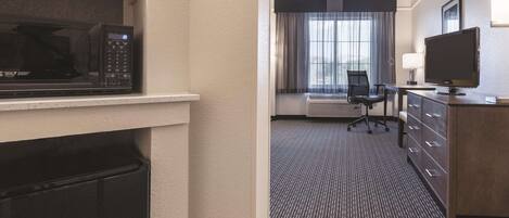 Habitación de hotel con microondas, escritorio con silla, televisor y un amplio ventanal con cortinas.