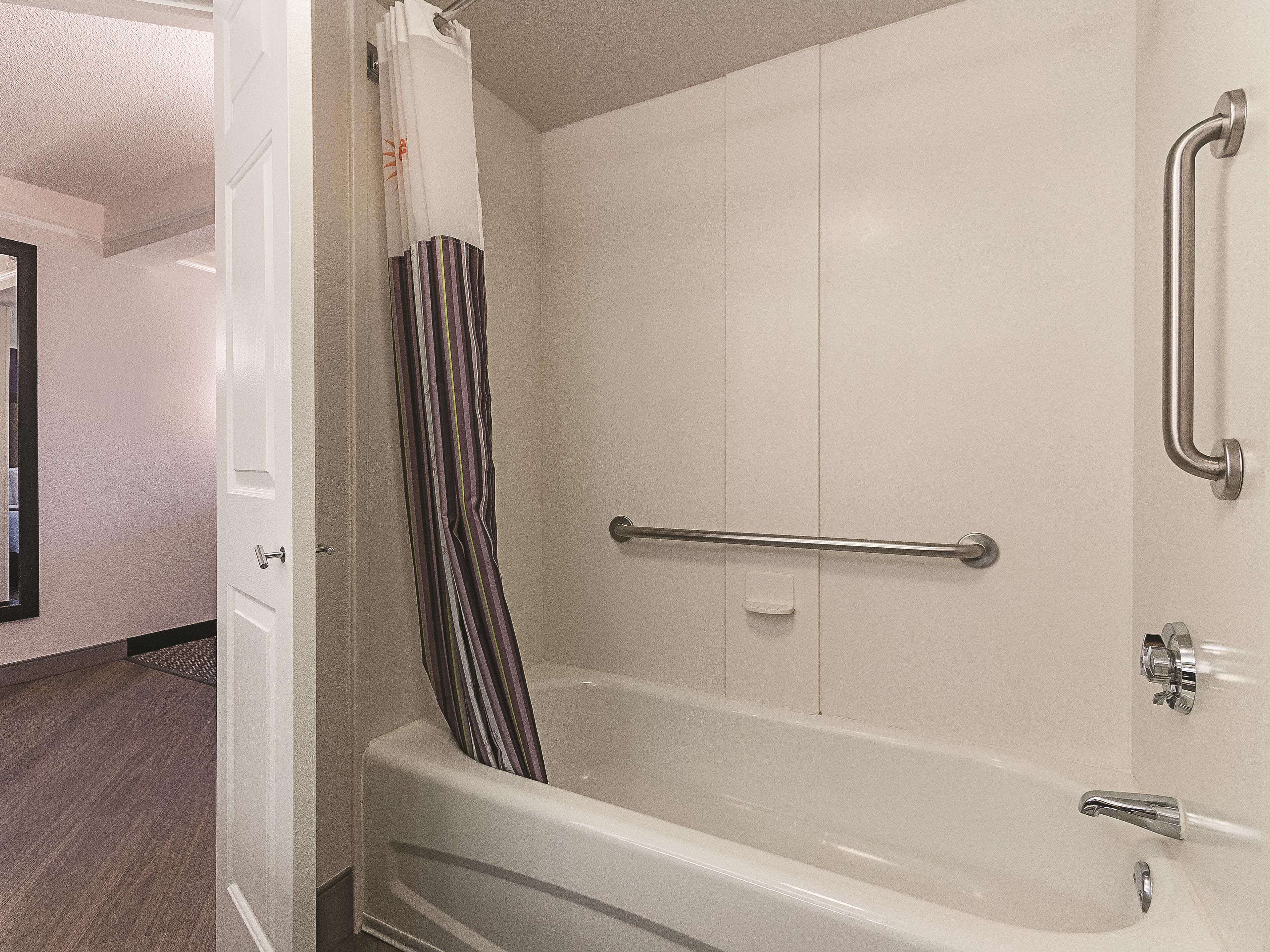 A bathroom with a bathtub, a shower with a grab bar, and a striped shower curtain.