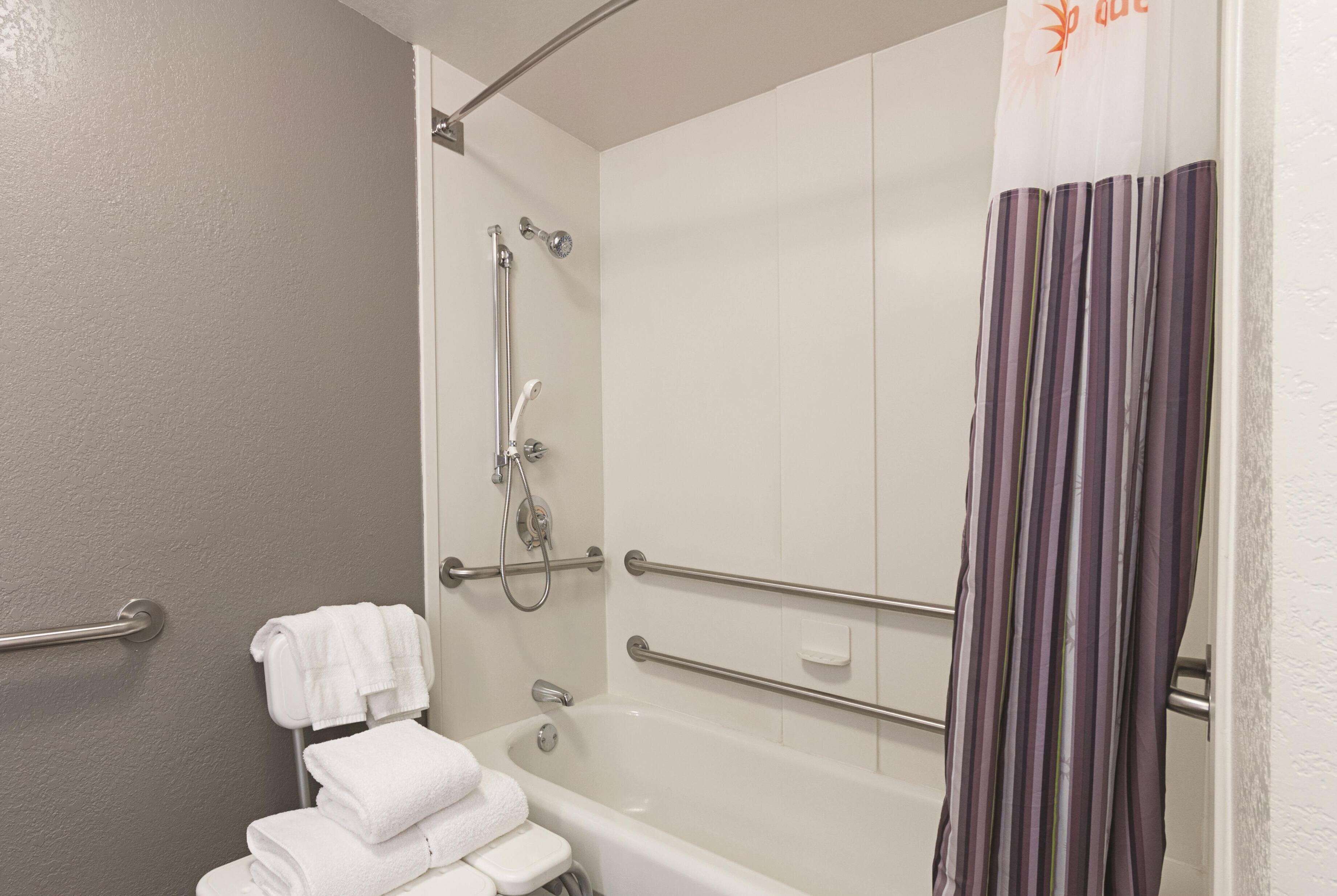 Ein Badezimmer mit Badewanne, Dusche und Toilette. Es gibt Handläufe und einen Handtuchhalter.