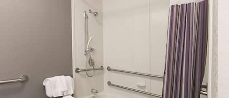 Ein Badezimmer mit Badewanne, Dusche und Toilette. Es gibt Handläufe und einen Handtuchhalter.