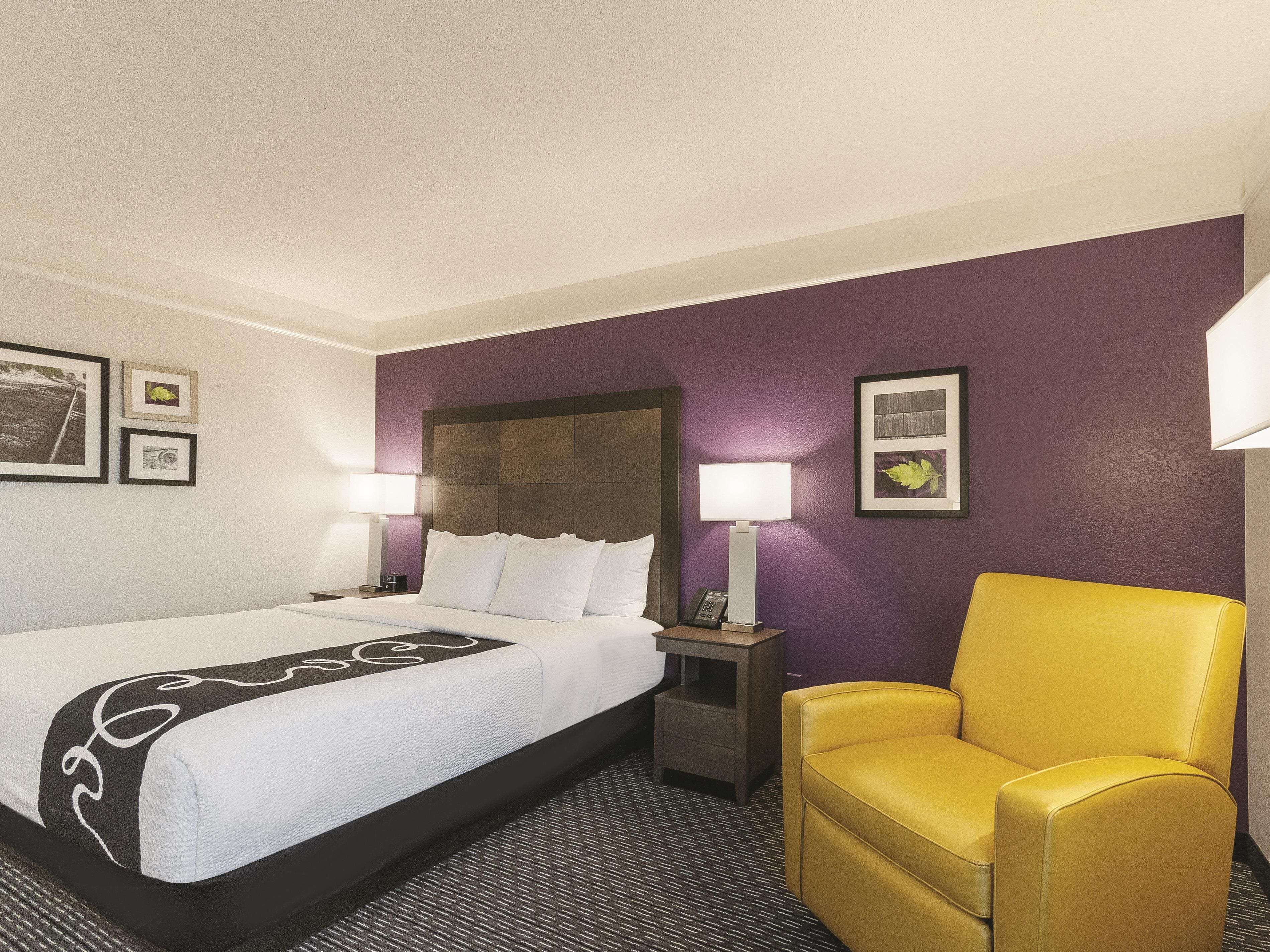 A hotel room with a bed, a nightstand, a chair, and wall decorations.