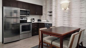 A modern kitchen with stainless steel appliances, dark wooden cabinets, and a dining area with a wooden table and chairs. - Residence Inn By Marriott Las Vegas/Green Valley (Henderson)
