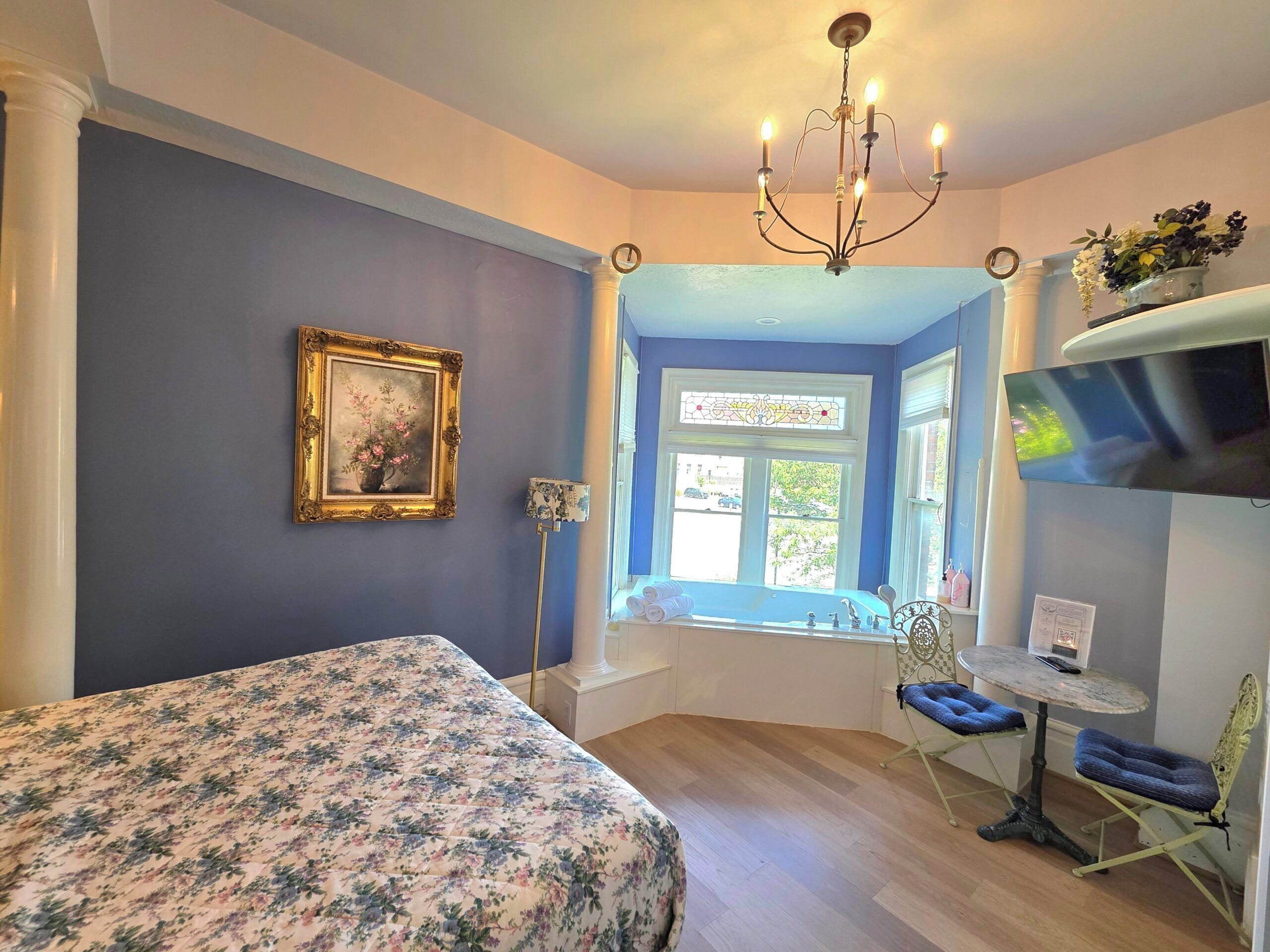 Una camera da letto con un letto, un lampadario, una finestra vista, un quadro e una TV.