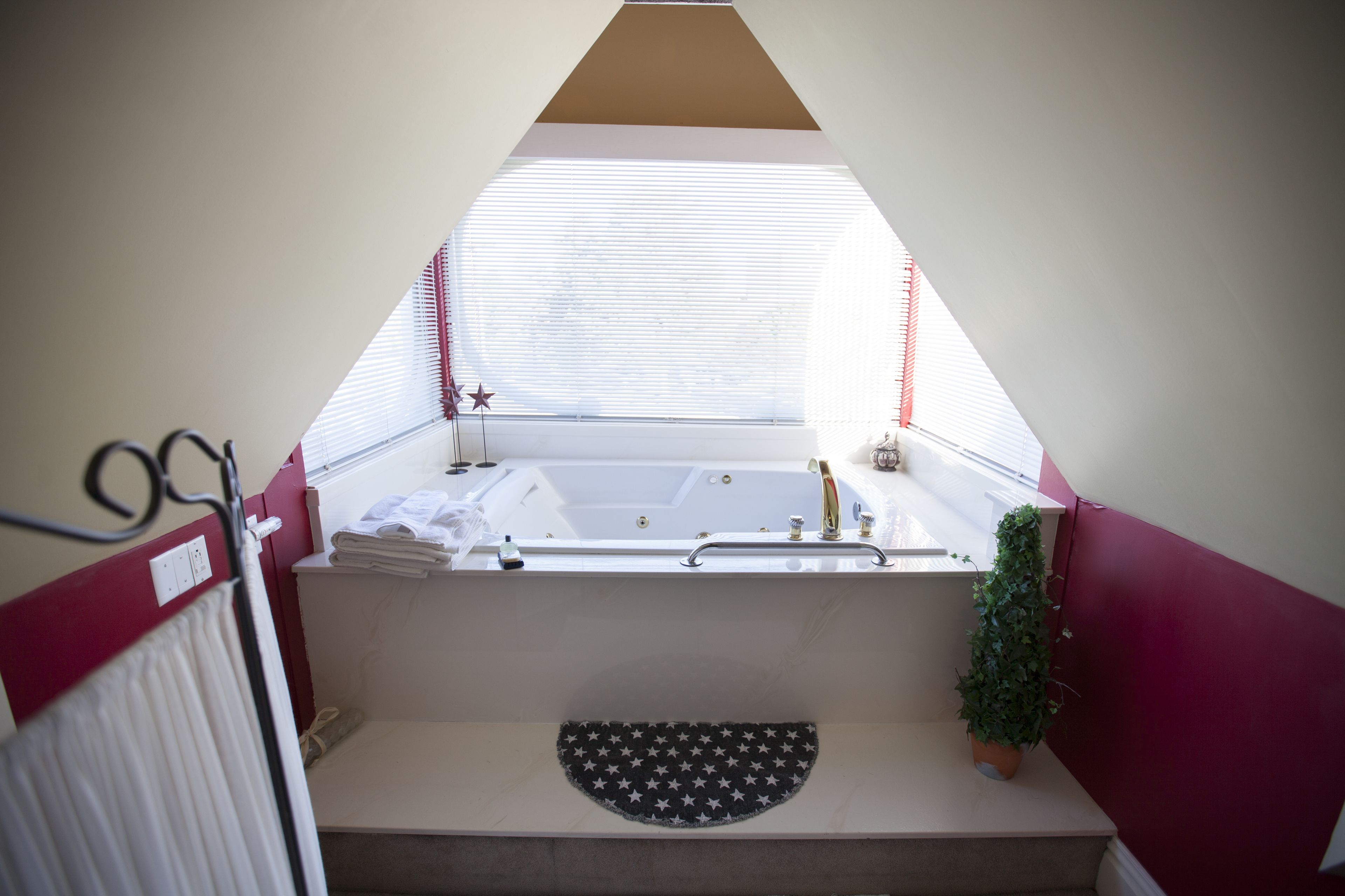 Un baño con bañera, un perchero, una planta pequeña y una ventana con persianas.