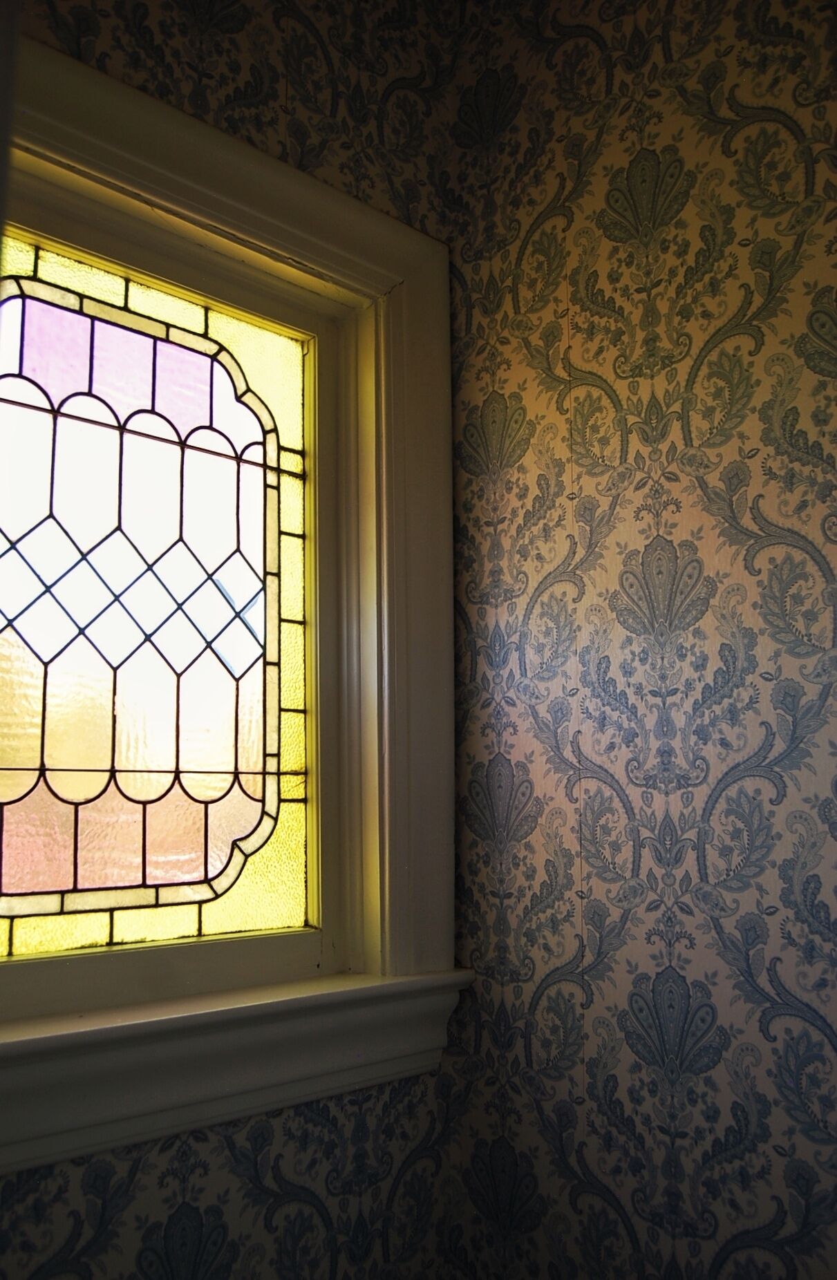 A window with a stained glass design and a patterned wallpaper.