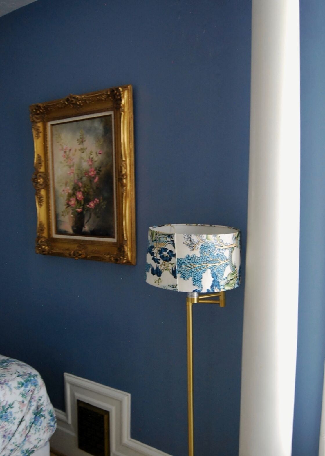 Une pièce avec un mur bleu, un tableau encadré représentant des fleurs et un lampadaire doté d’un abat-jour à motifs floraux.