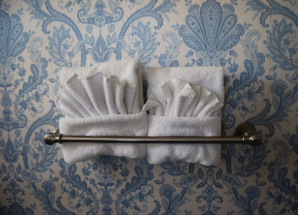 A bathroom with a towel rack holding two folded towels against a patterned wallpaper. - Hines Mansion (Provo)