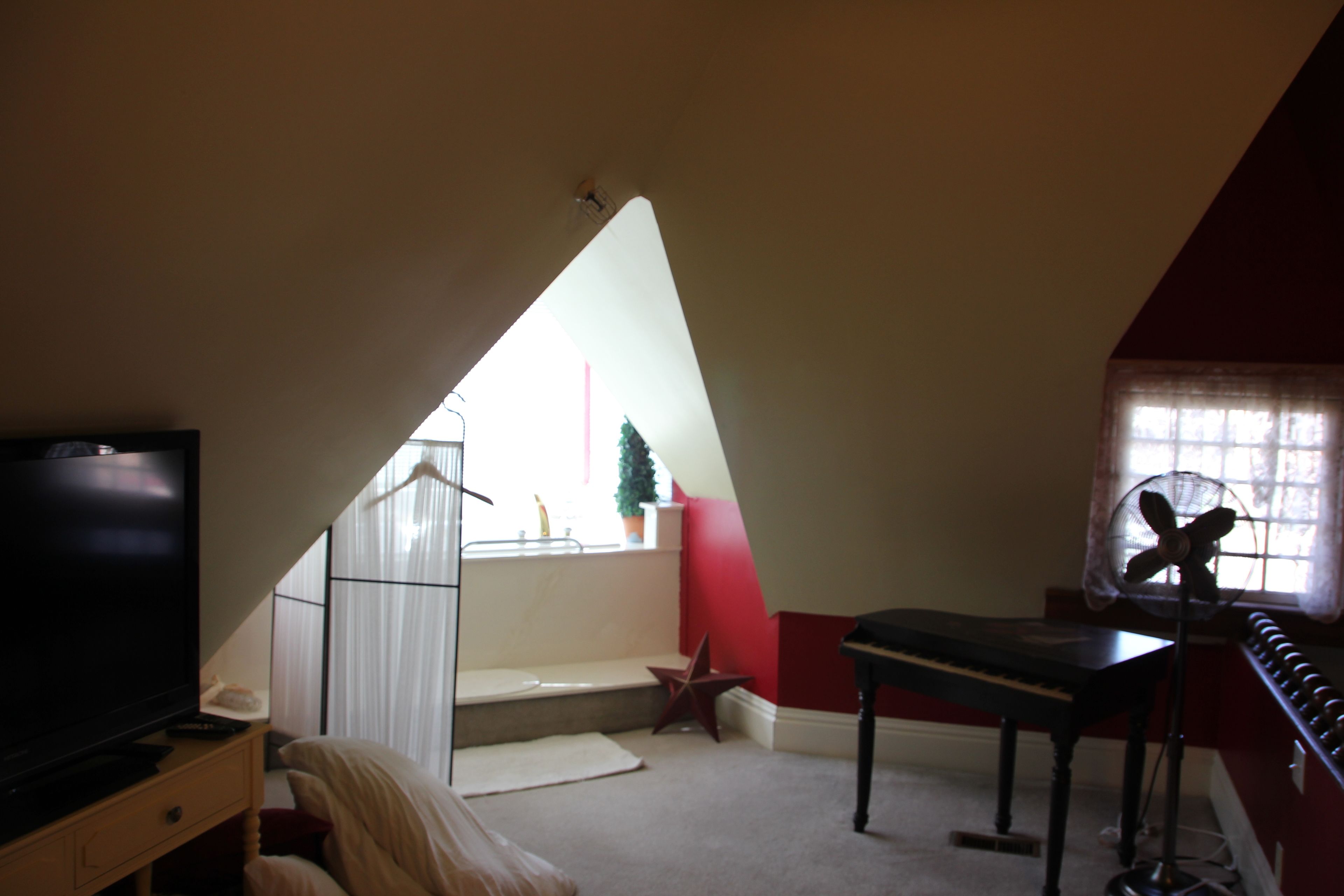 Una stanza con televisione, pianoforte, ventilatore e una scala che porta a un balcone.
