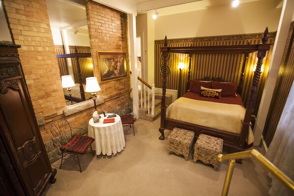 Classic four-poster bed positioned near a brick wall and mirror, with a small table and chair nearby.
