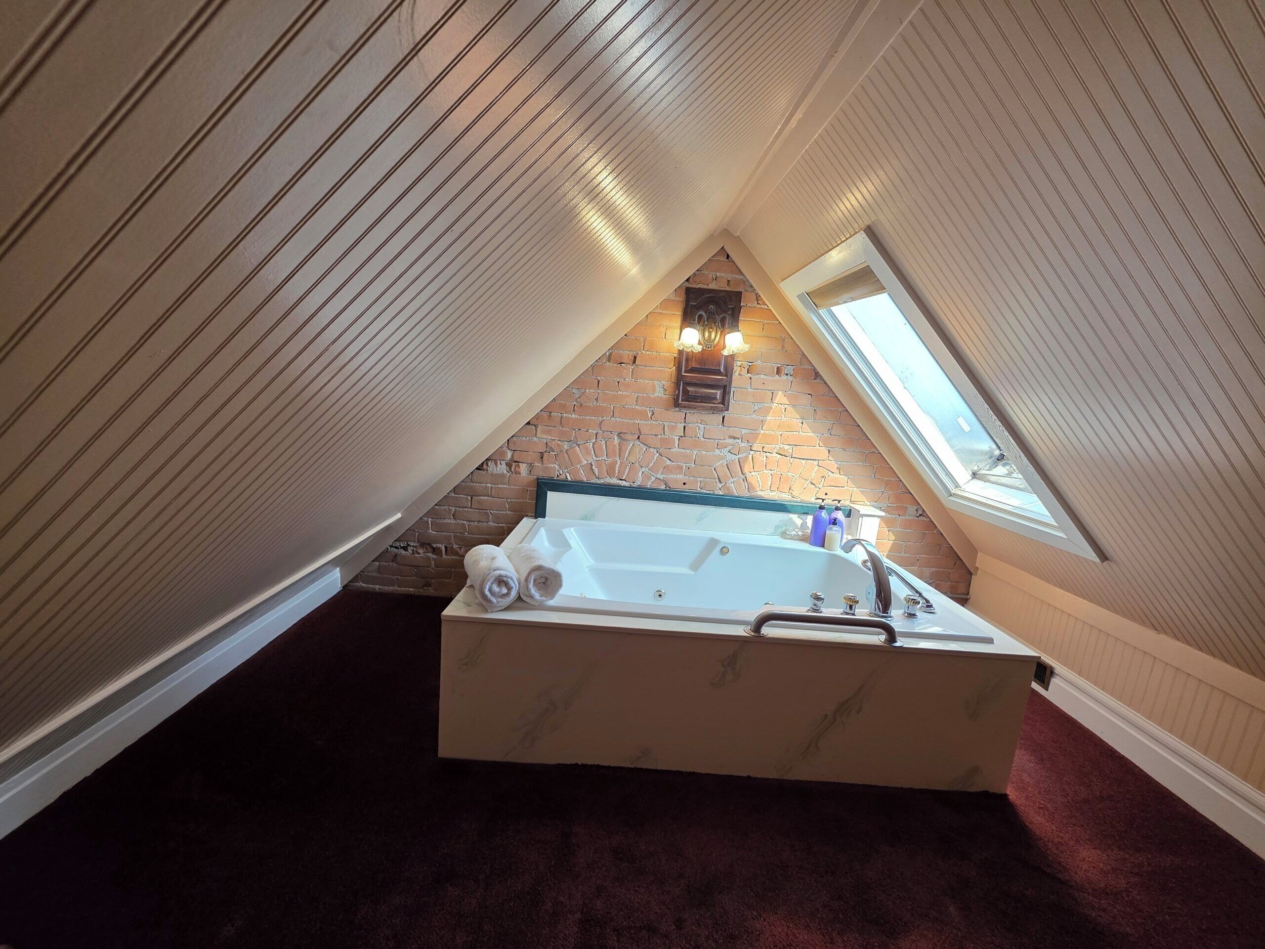 A room with a sloped ceiling, a brick wall, a large bathtub, and a skylight.