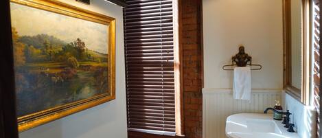 A bathroom with a white sink, a mirror, and a framed landscape painting on the wall.