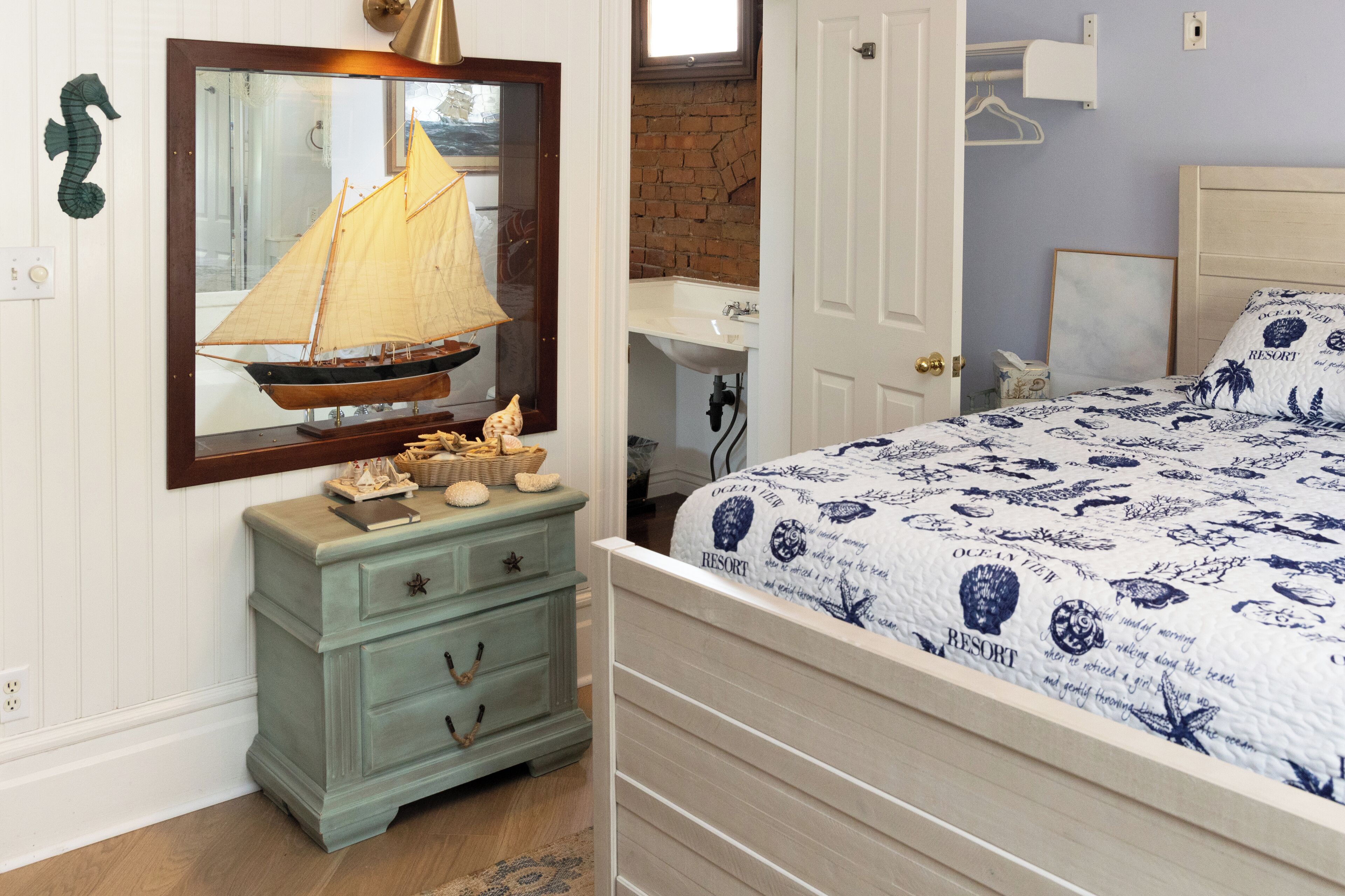 A bedroom with a bed, dresser, and a mirror with a sailboat.