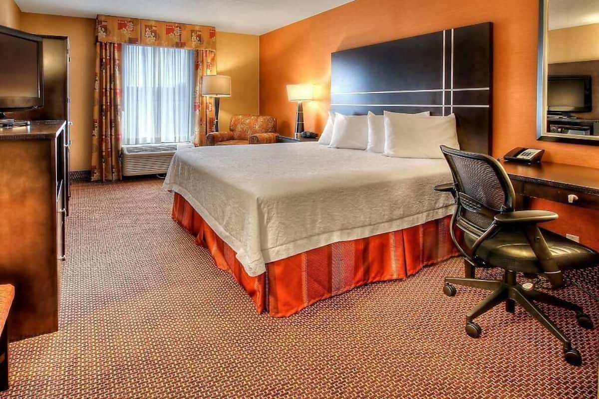 Ein Hotelzimmer mit einem großen Bett, einem Schreibtisch mit Stuhl, einem Fernseher und einem Spiegel.