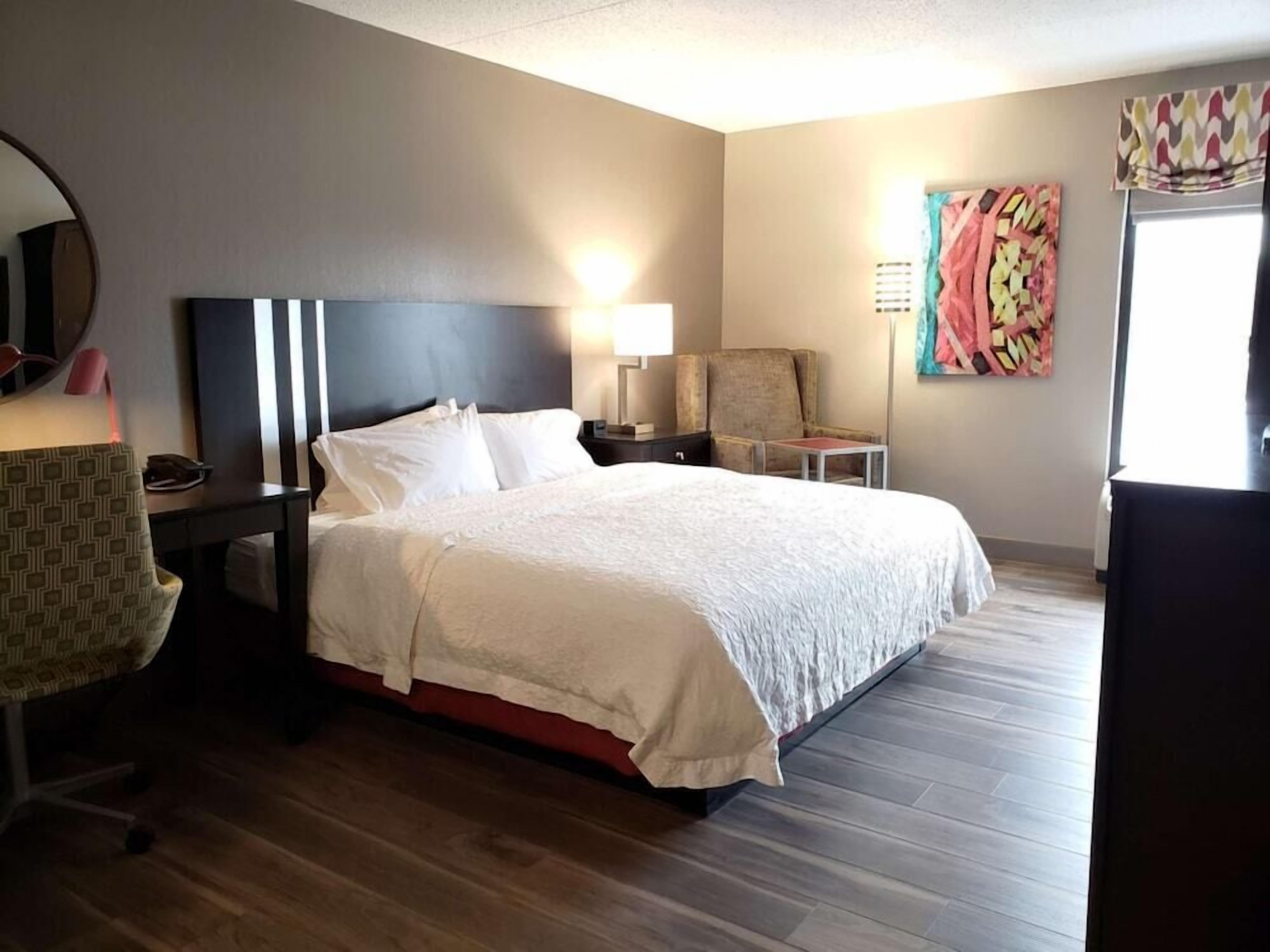 Una camera d'albergo con un letto, una sedia, una scrivania, una lampada e un quadro appeso al muro.