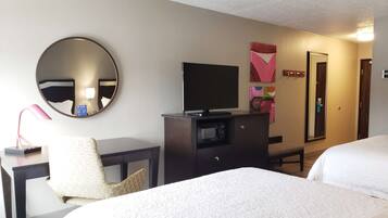 A hotel room with two beds, a desk with a computer, a TV, a mirror, and a door.
