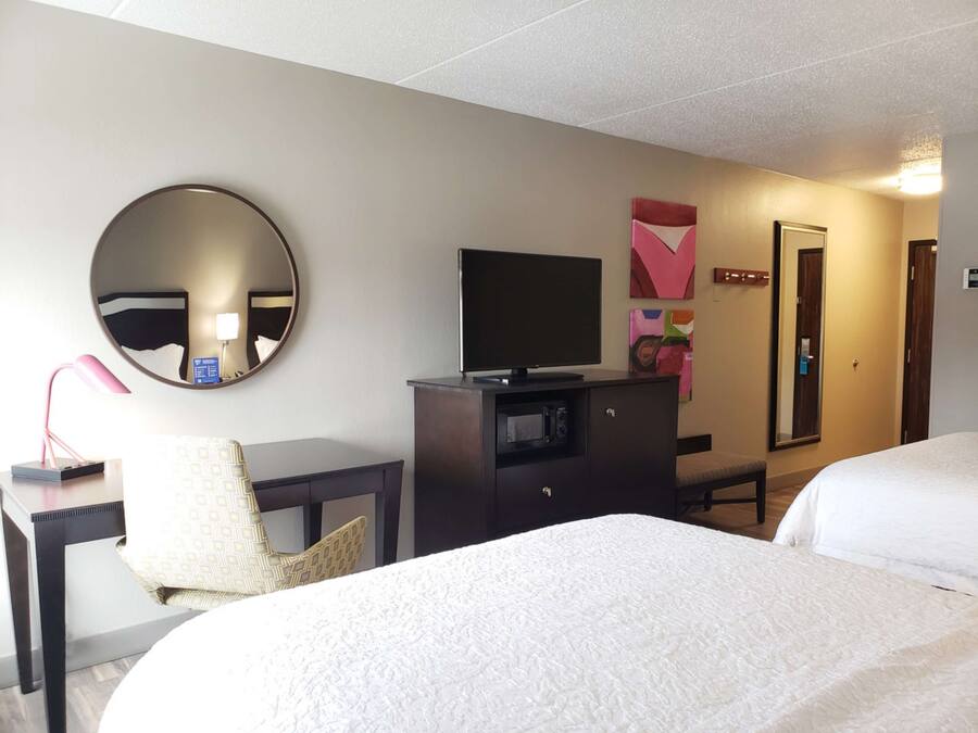 A hotel room with two beds, a desk with a computer, a TV, a mirror, and a door.