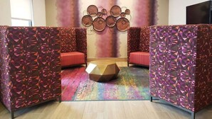 Una habitación con dos zonas de asientos acolchadas en rojo, separadas por una partición de diseño geométrico y colorido. Se observa un adorno circular montado en la pared sobre los asientos.