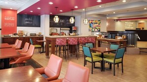Un restaurante con zona de bar, mesas y sillas, y una cocina al fondo.