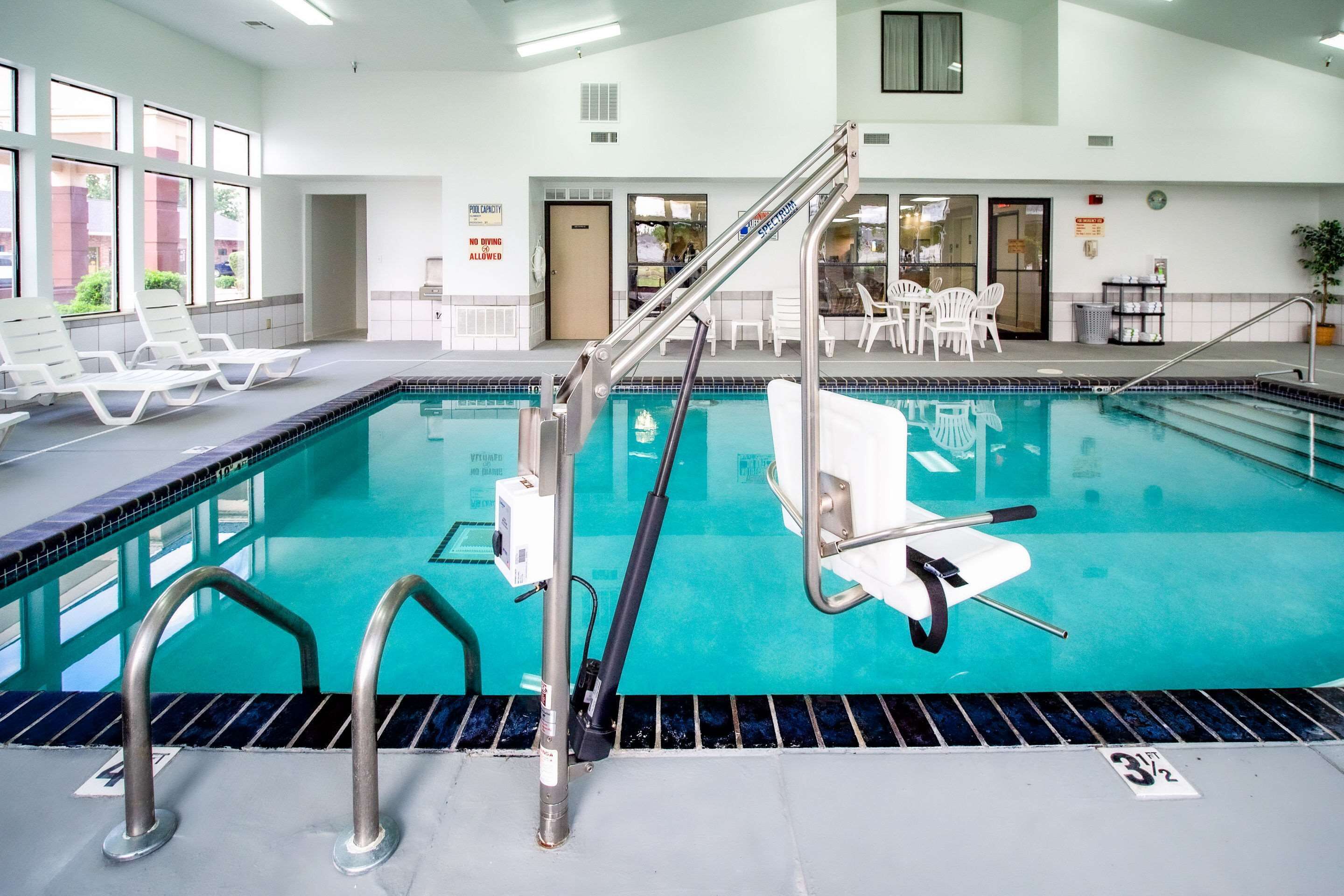Une piscine intérieure à l’eau claire, dotée de rampes de sécurité en métal et de chaises longues blanches.