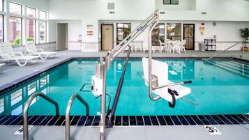 Une piscine intérieure à l’eau claire, dotée de rampes de sécurité en métal et de chaises longues blanches.