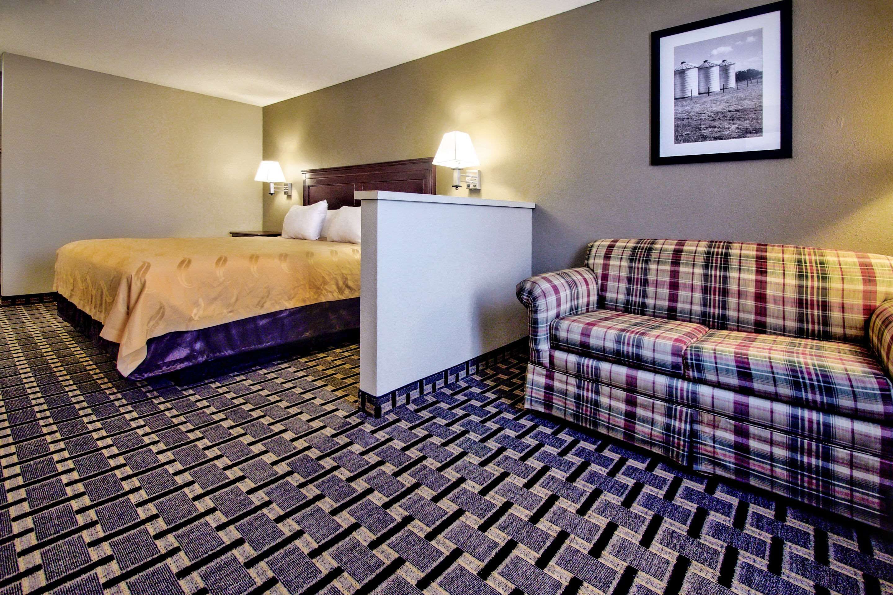 A hotel room with a bed, a small white table, a couch, and a patterned floor.