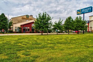 A Quality Inn hotel with a red facade, a grassy lawn, and trees.