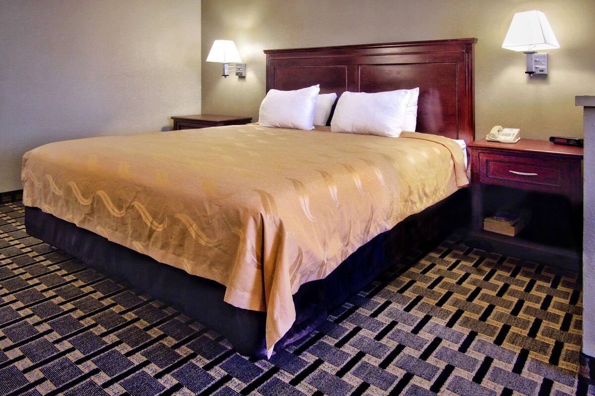 A hotel room with a large bed, two bedside tables, a nightstand, and a lamp on each side.
