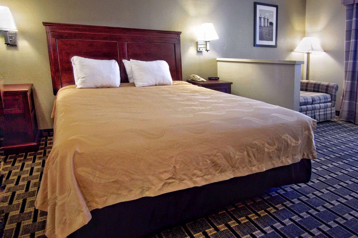 A large bed with a wooden headboard, two bedside tables, a lamp, and a framed picture on the wall.