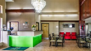 A hotel lobby with a reception desk, a chandelier, a green reception area, and seating arrangements.